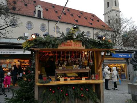 Das Bild zeigt einen Weihnachtsmarktstand namens "Mandelhans" vor der Heilig-Geist-Kirche in München.
