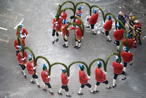 Das Bild zeigt den traditionellen bayerischen Schäfflertanz (Küfertanz), ein Zunfttanz, der nur alle sieben Jahre aufgeführt wird. Der Brauch geht auf das Jahr 1517 zurück, als die Pest in München wütete und die Schäffler (Fassmacher) mit diesem Tanz die verängstigte Bevölkerung wieder aus den Häusern locken und Lebensfreude verbreiten wollten.