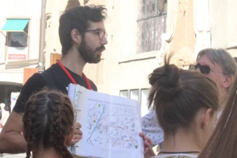 Das Bild zeigt einen Reiseführer der im Rahmen einer Stadtführung einen Stadtplan verwendet um einer Gruppe von Touristen Sehenswürdigkeiten und Routen zu zeigen.